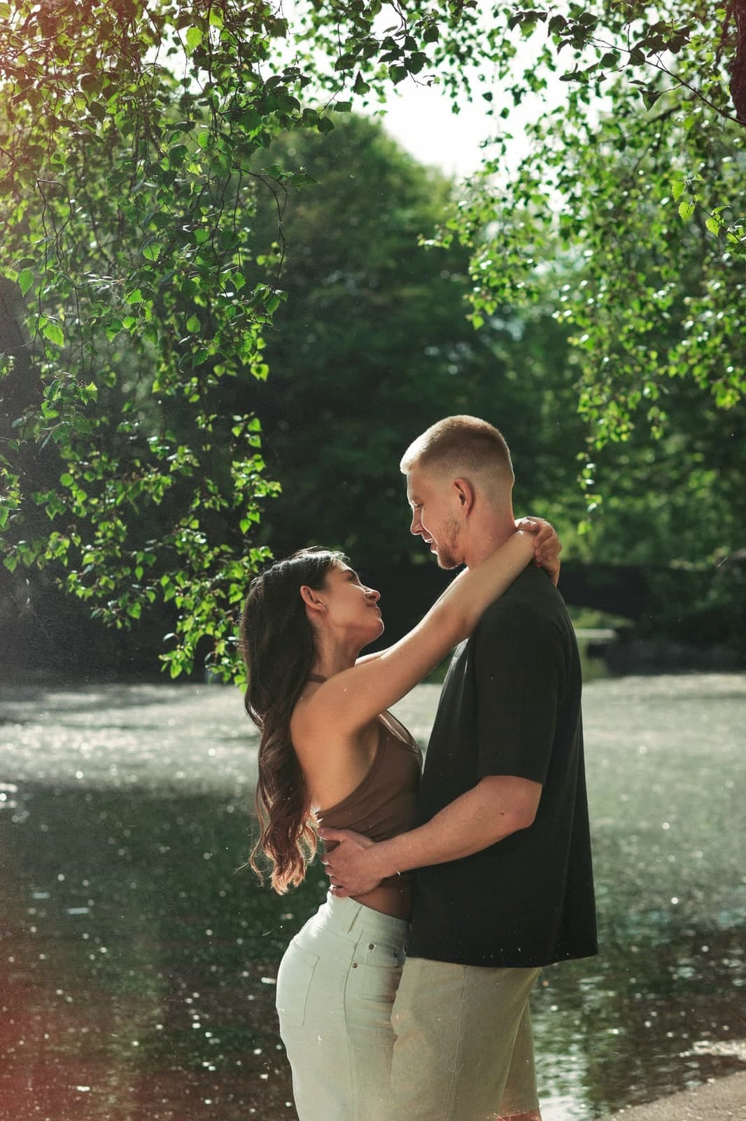 Couple embracing by a sunlit pond under the trees