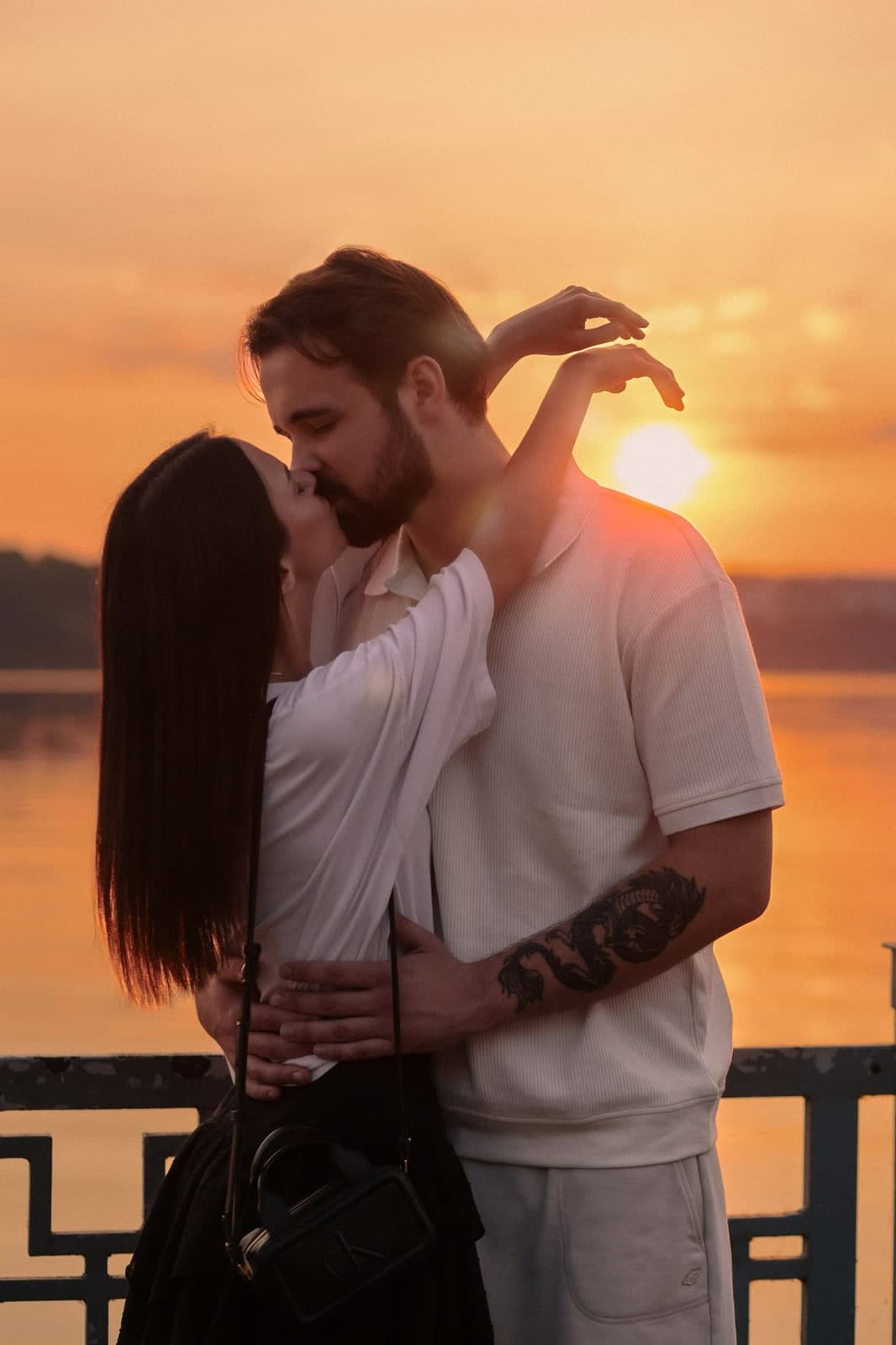 A kiss at sunset by the water, one arm raised against the sun