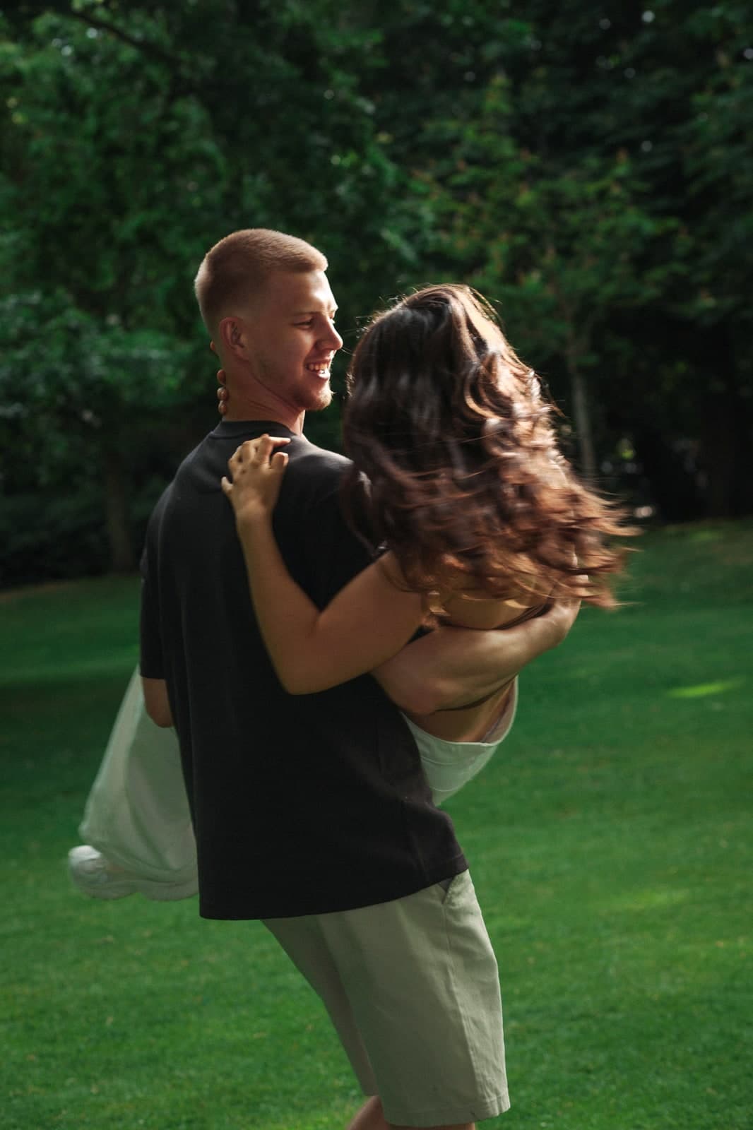 Couple spinning in each other's arms on a sunlit lawn, hair flying