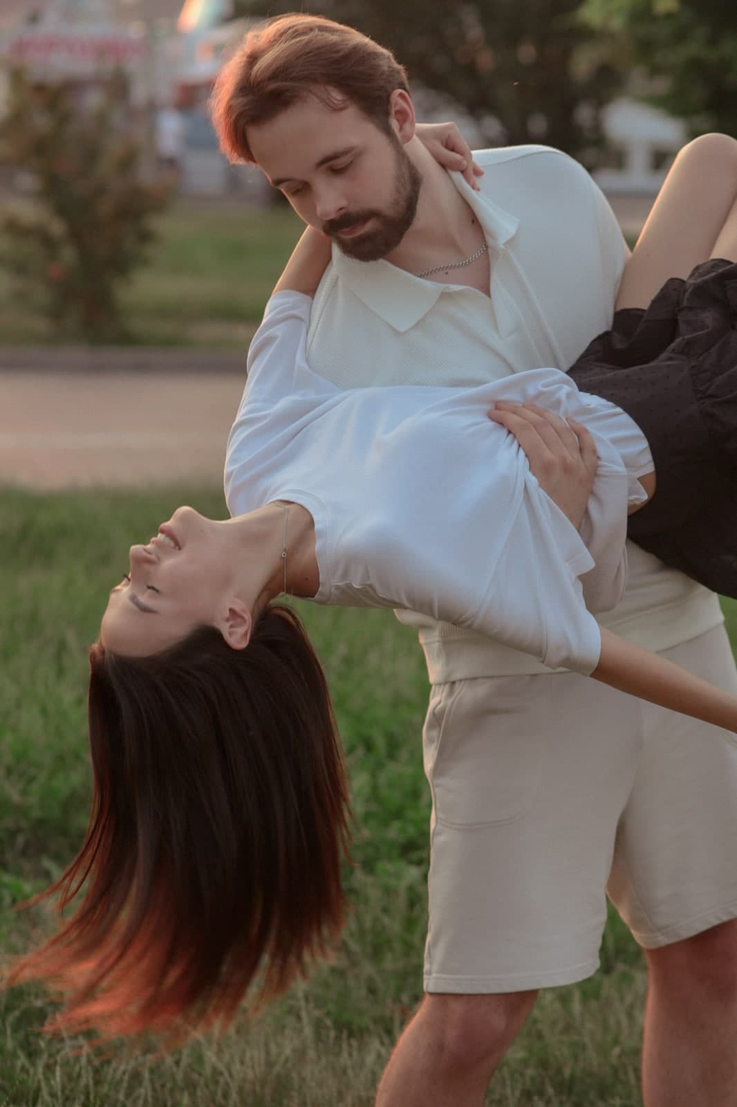 Couple in pale summer clothes, one dipping the other backwards over the grass