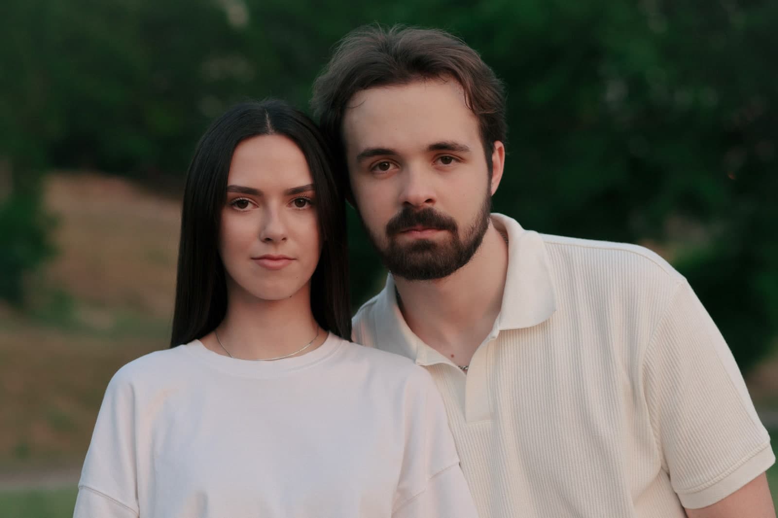 Couple cheek to cheek in white T-shirts, looking into the camera in a park