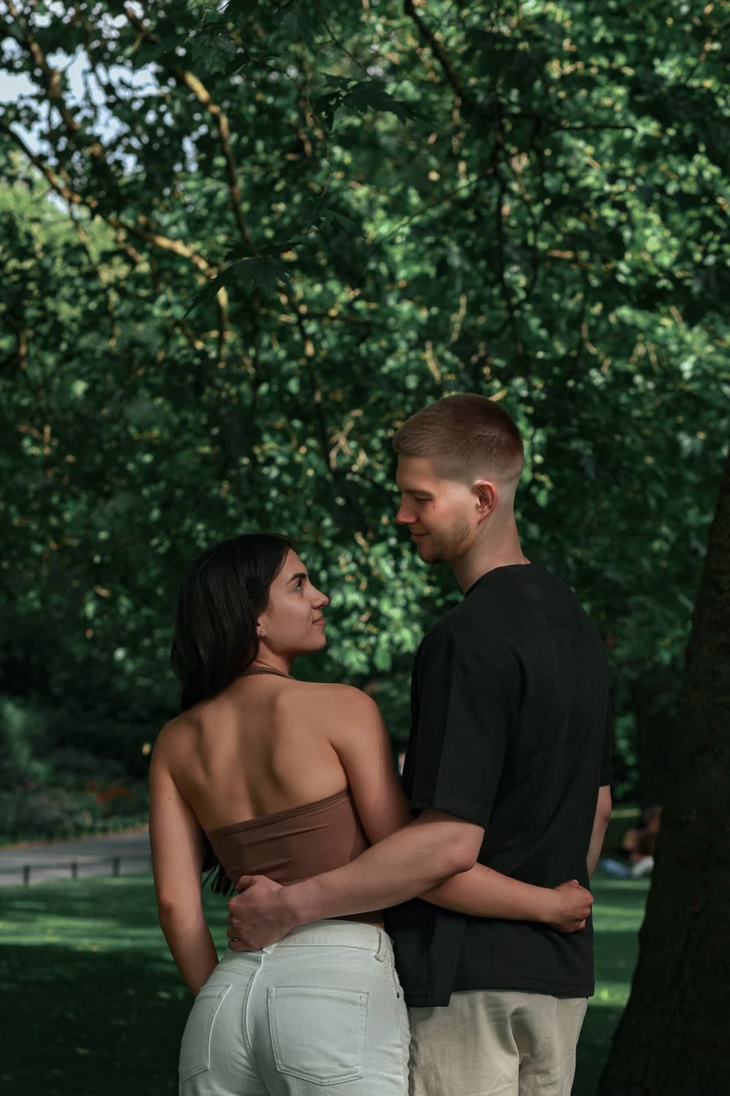 Couple seen from behind, arms around each other, sharing a look under the trees
