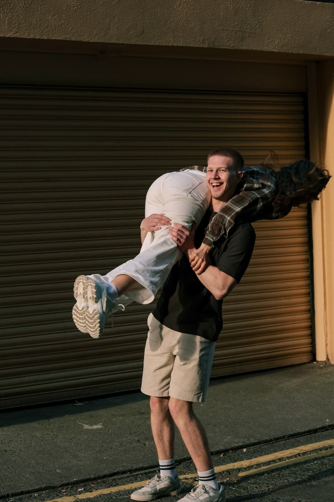 Carrying a laughing partner over one shoulder in front of a shop shutter