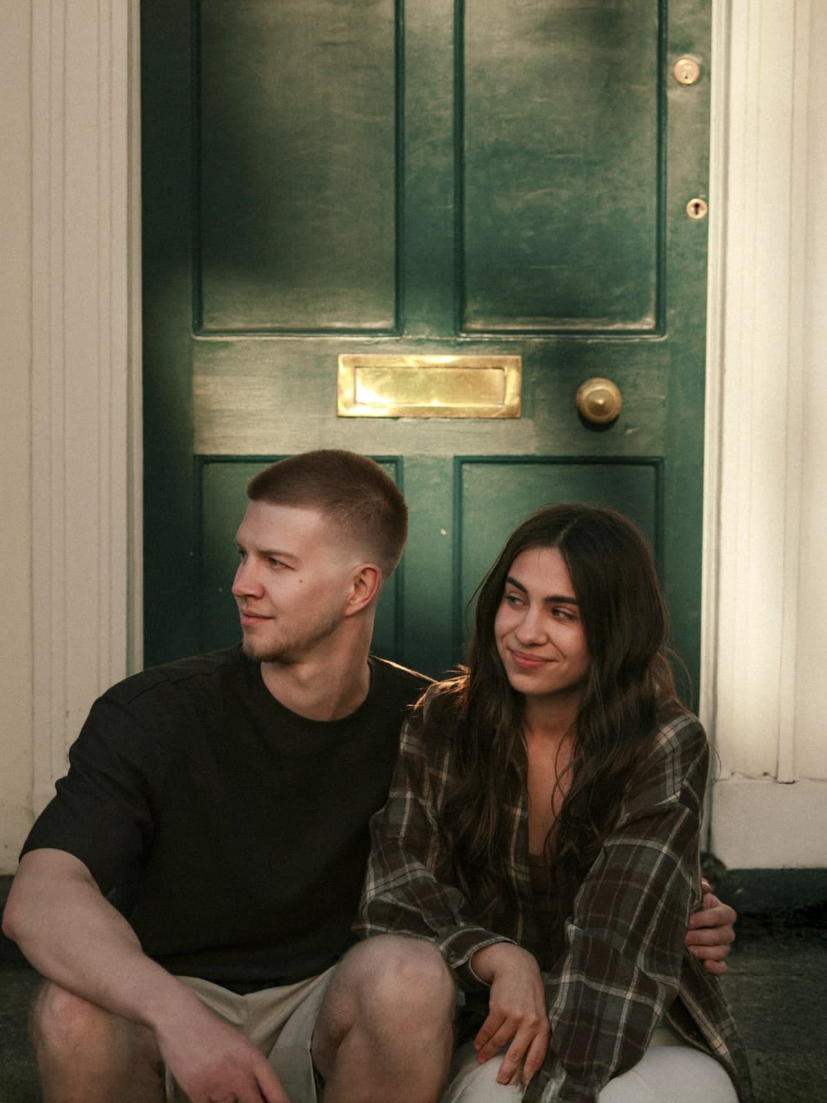 Couple sitting on the step of a green Georgian door, smiling at each other