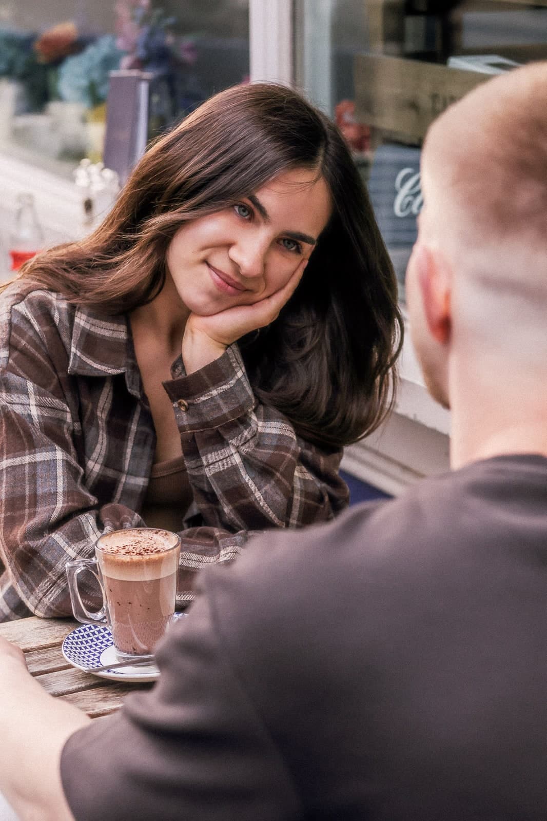 Chin in hand, smiling across a café table over a hot chocolate