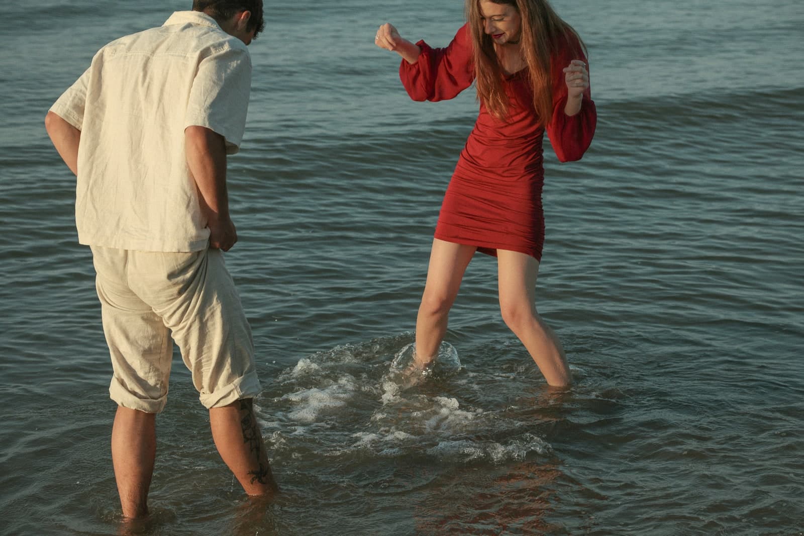 Couple splashing barefoot in the shallows, in a red dress and white linen