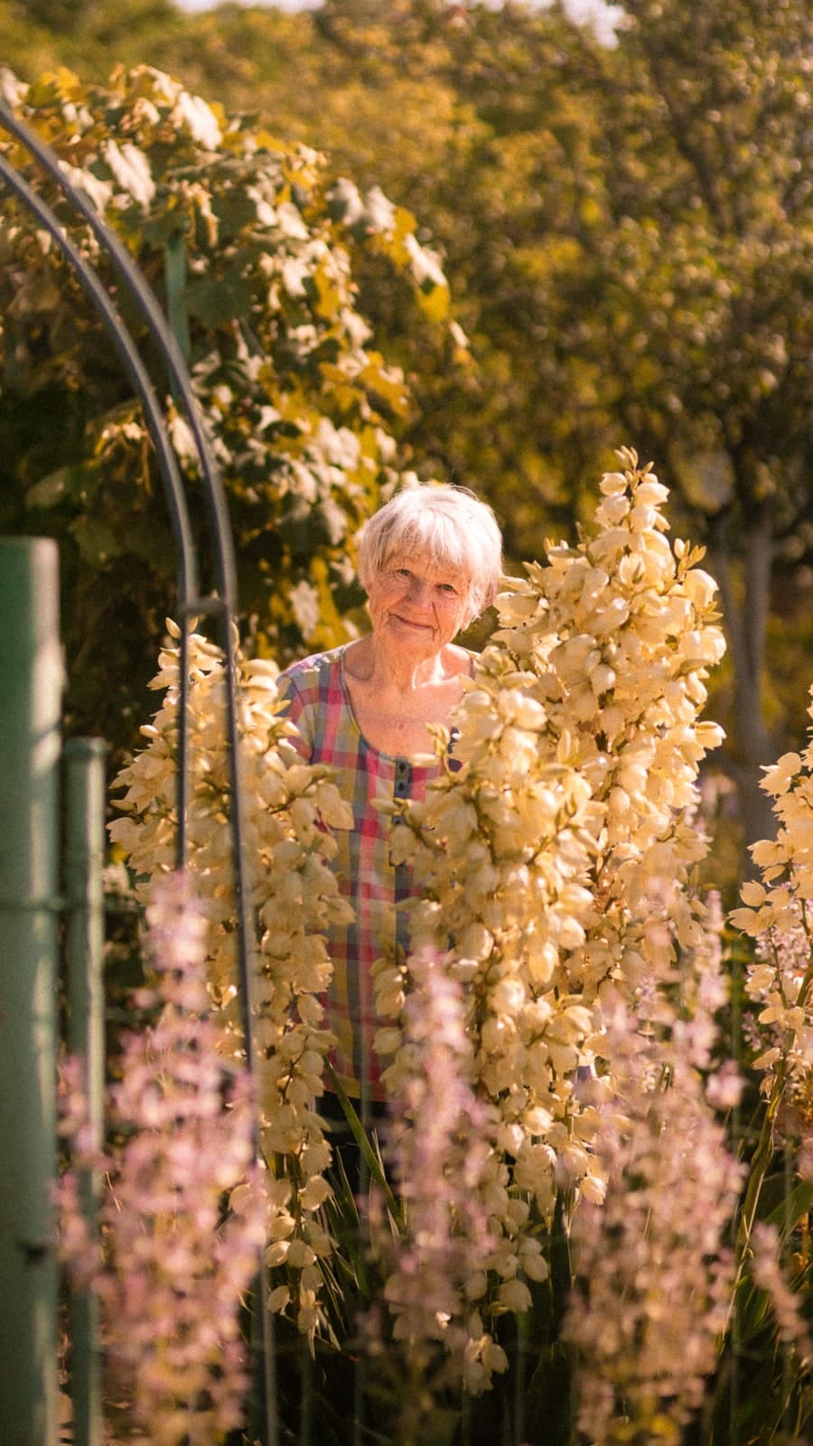 Smiling behind tall cream yucca blooms by a garden arch