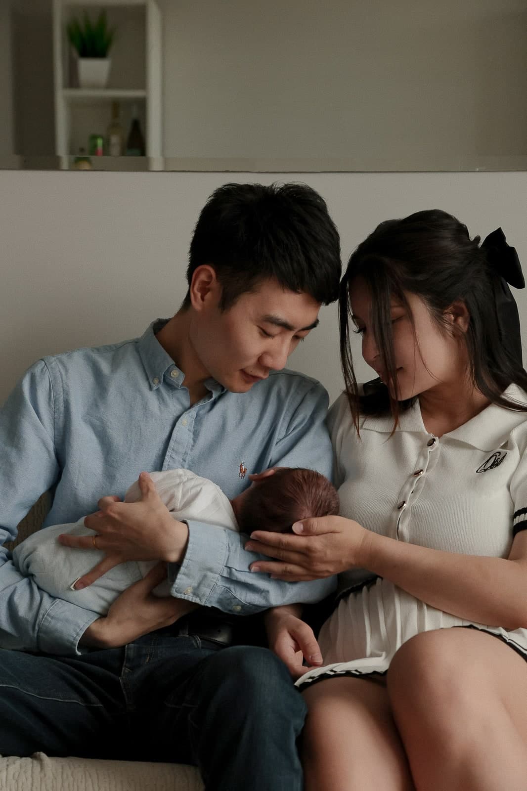 Both parents leaning over their newborn on the sofa at home