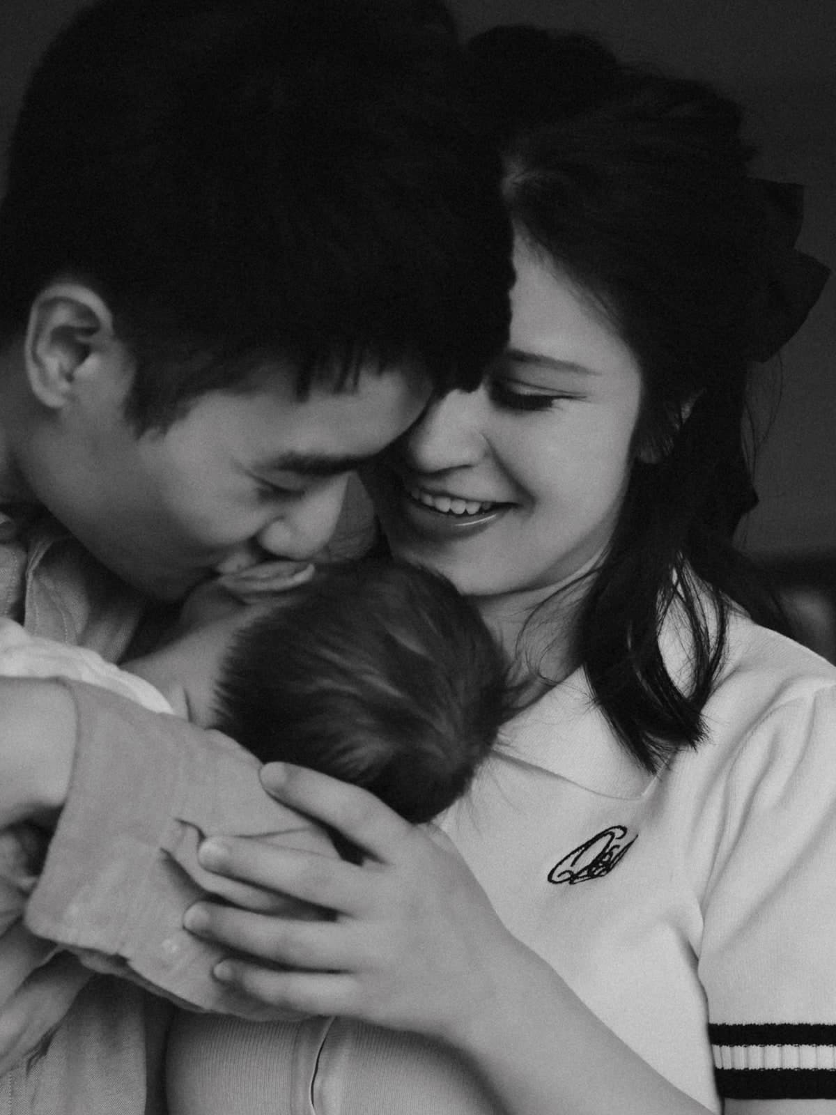 Black-and-white close-up of both parents cuddling their newborn, cheek to cheek