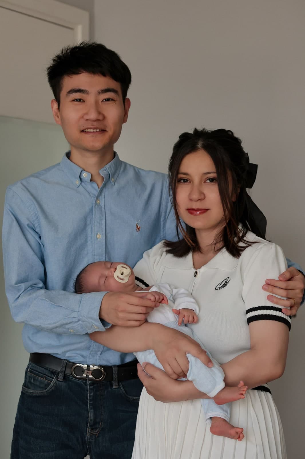Family portrait at home: both parents standing together, holding their newborn