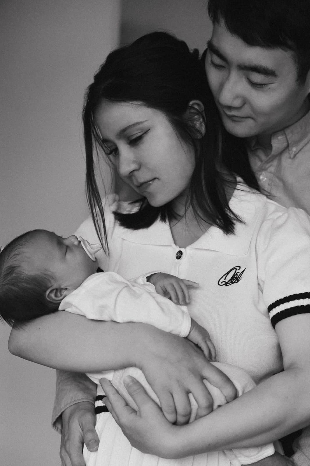 Black-and-white portrait of both parents holding their sleeping newborn together