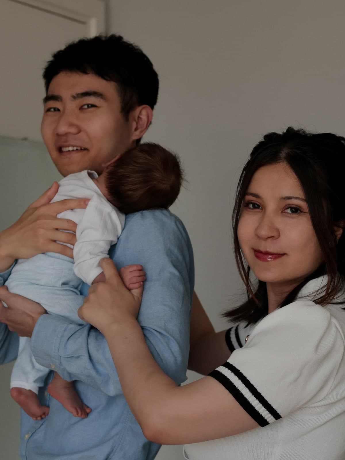 Laughing together at home while the newborn snuggles into a parent's shoulder