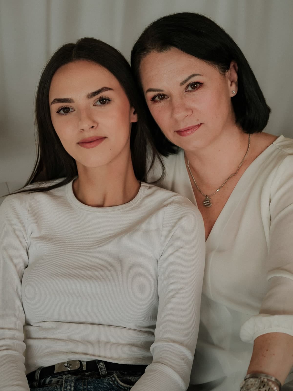 Two generations cheek to cheek in cream tops, looking into the camera