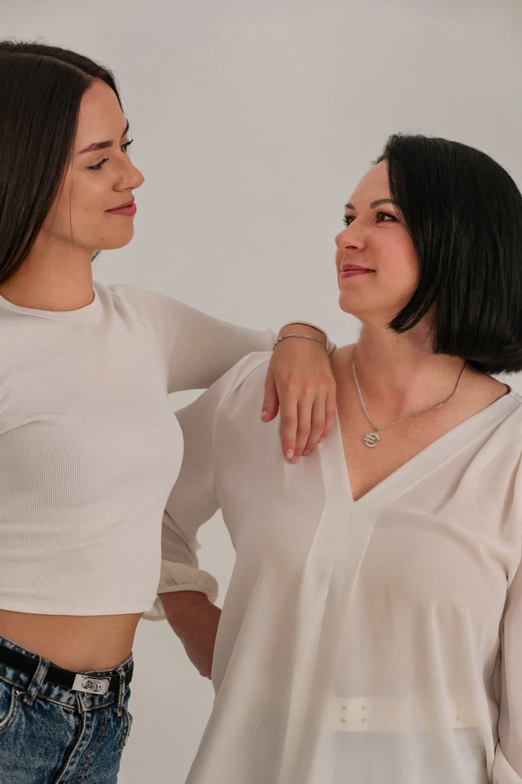 Two generations in white, one leaning on the other's shoulder, smiling at each other