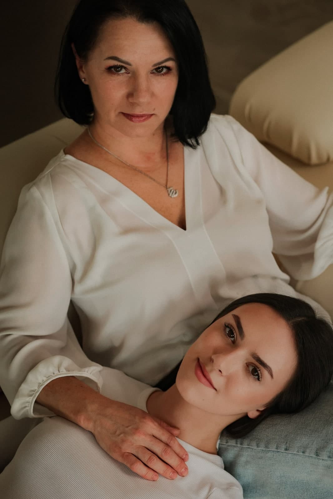On a cream sofa, one head resting in the other's lap, both looking at the camera