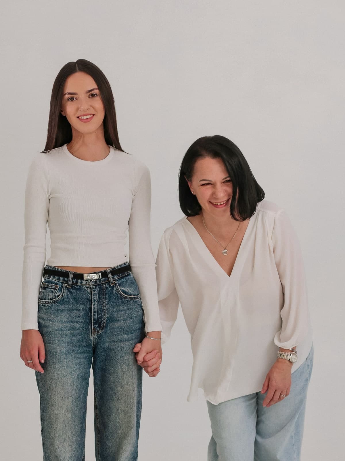 Two generations holding hands and laughing in jeans and white tops, white studio wall