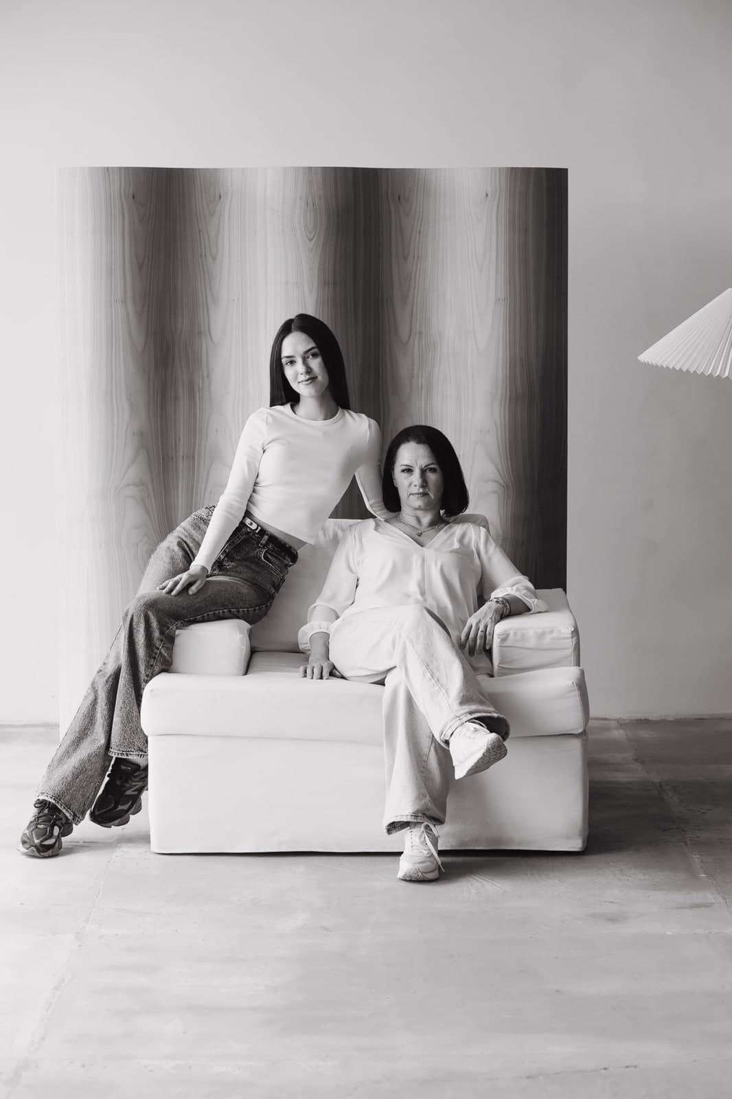 Black-and-white: two generations sitting together on a white armchair in a bright studio
