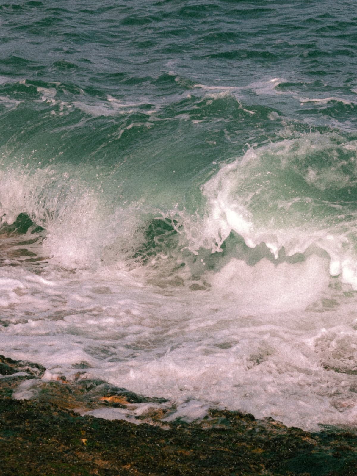 A green wave breaking white over dark rocks