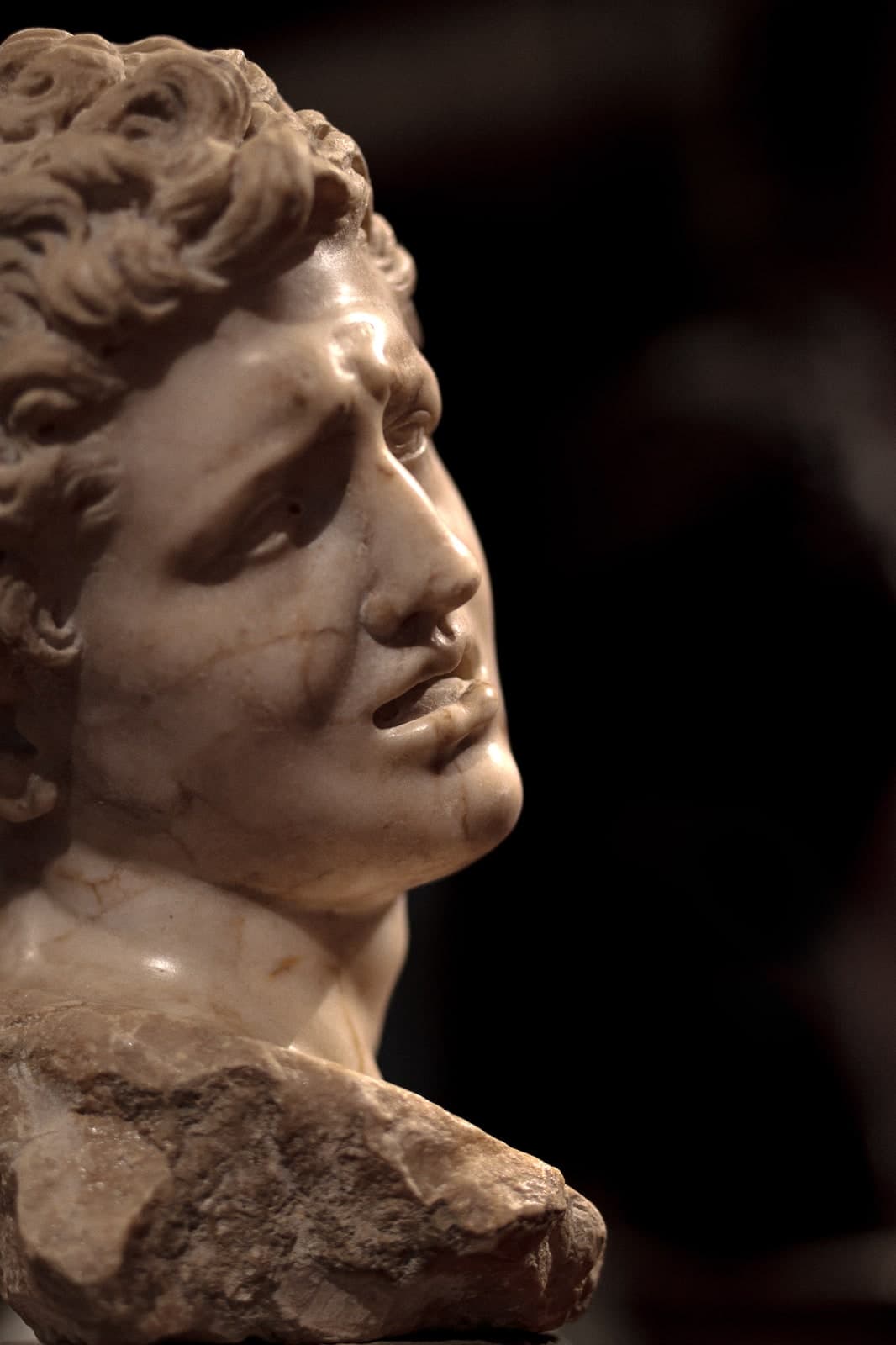 Marble bust of an anguished face, lit against the dark