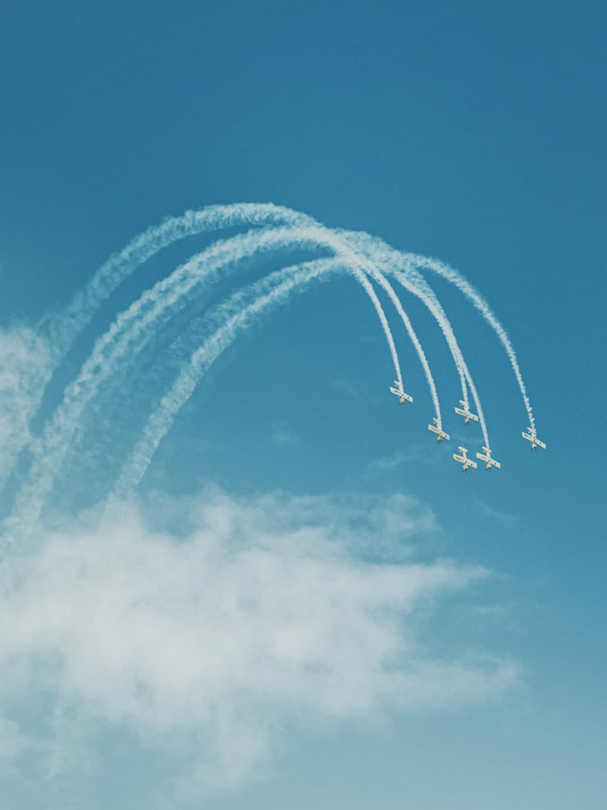 Aerobatic planes drawing white smoke arcs across a blue sky
