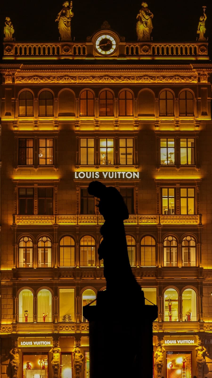 A statue in silhouette against an ornate façade lit gold at night