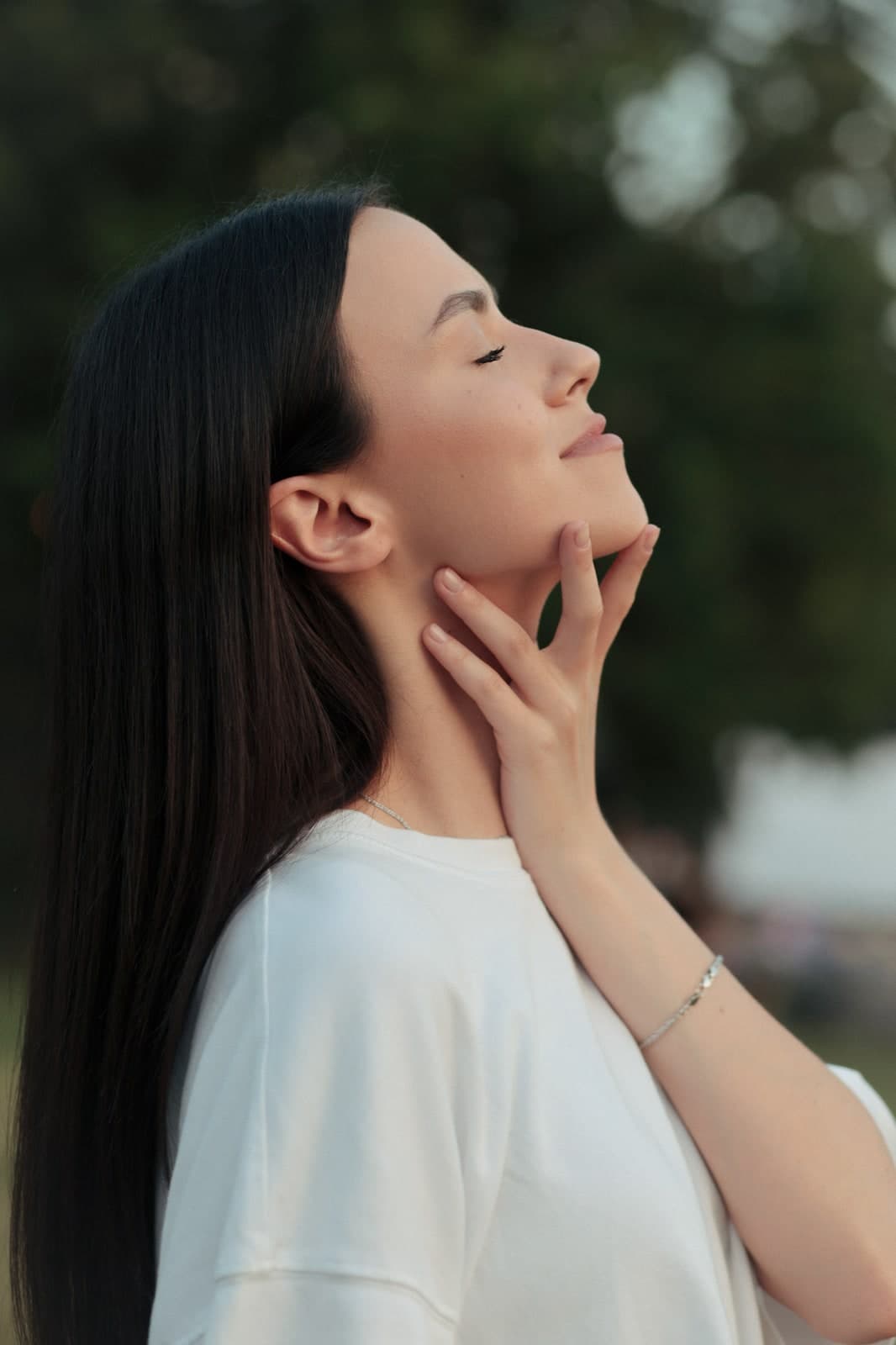 Profile with eyes closed and fingertips at the jaw, long dark hair, white T-shirt