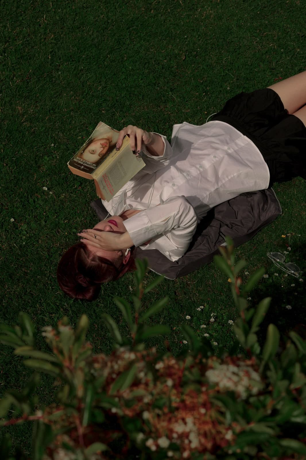 Lying on the grass with a book, a hand over the eyes, seen from above
