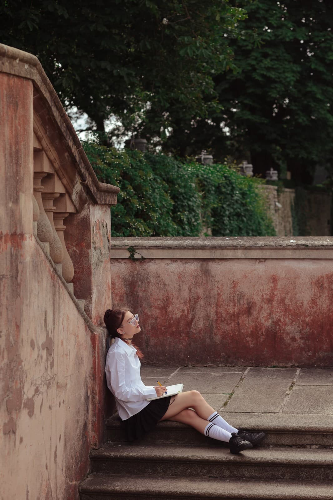 Sitting at the foot of old pink stone steps in a garden, looking up from a book