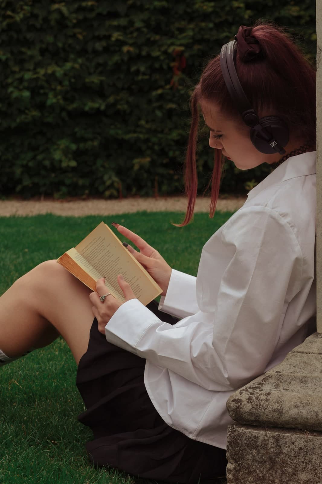 Reading in the grass with headphones on, back against a stone ledge