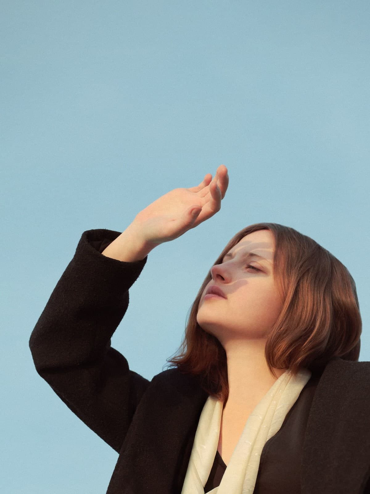 Shading the eyes with a raised hand against a clear blue sky