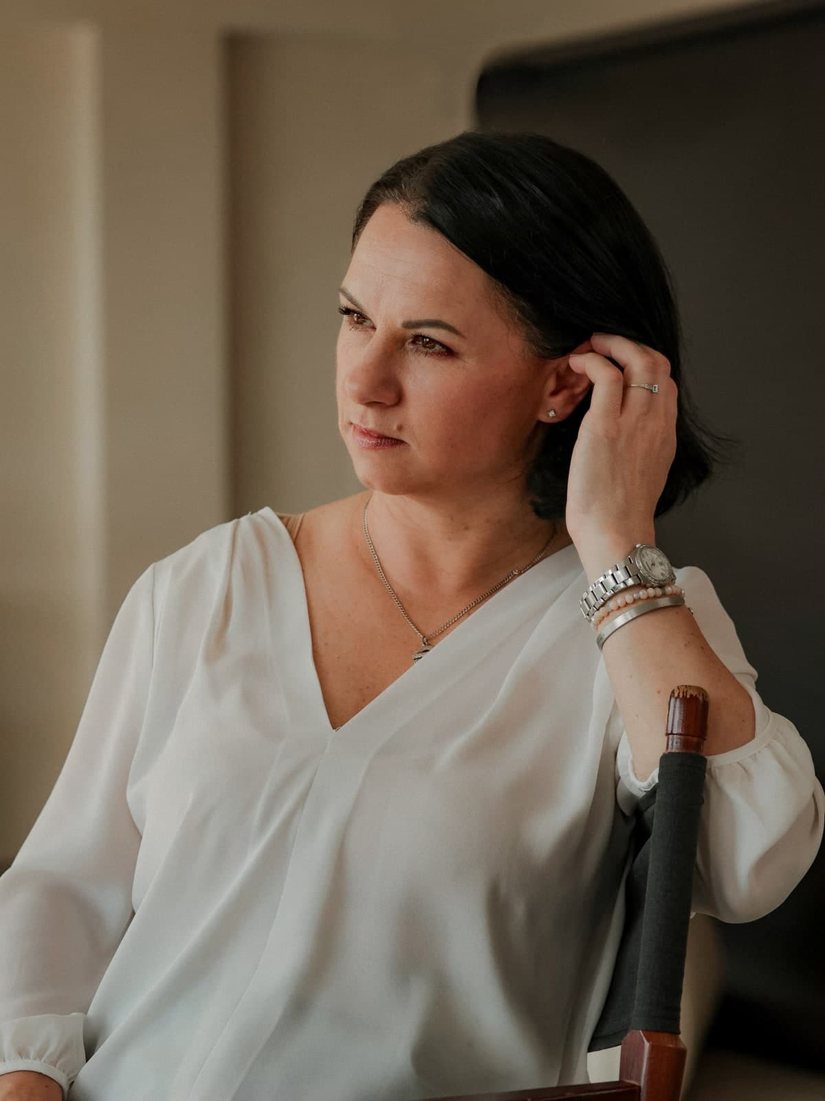 Tucking hair behind an ear and looking away, in a white blouse