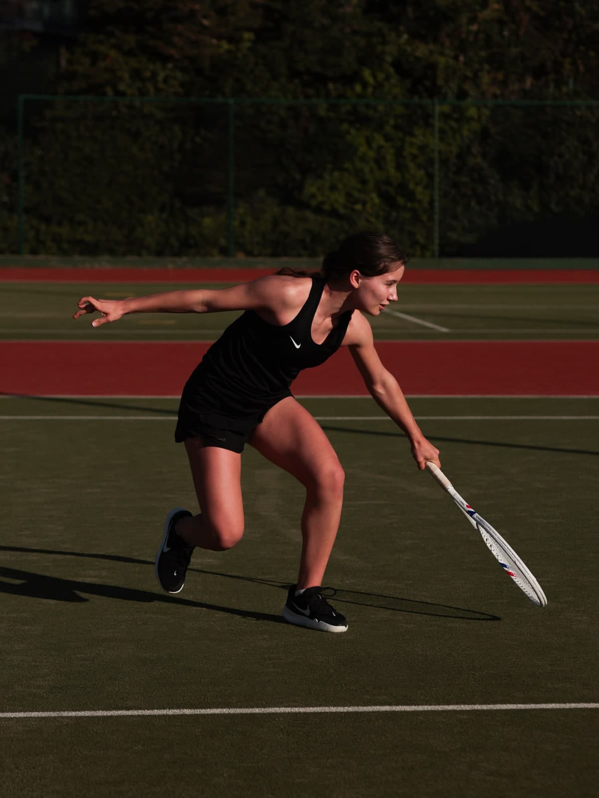 Lunging for a low ball on a red and green tennis court, in black sportswear