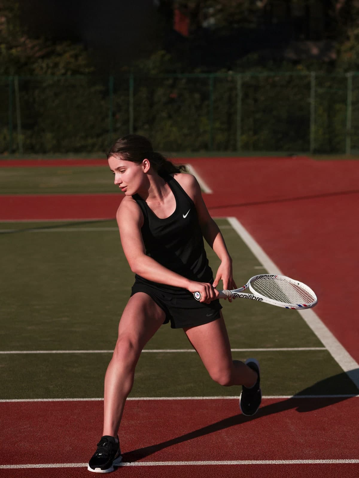 Ready for a forehand on a red tennis court, in a black tennis dress