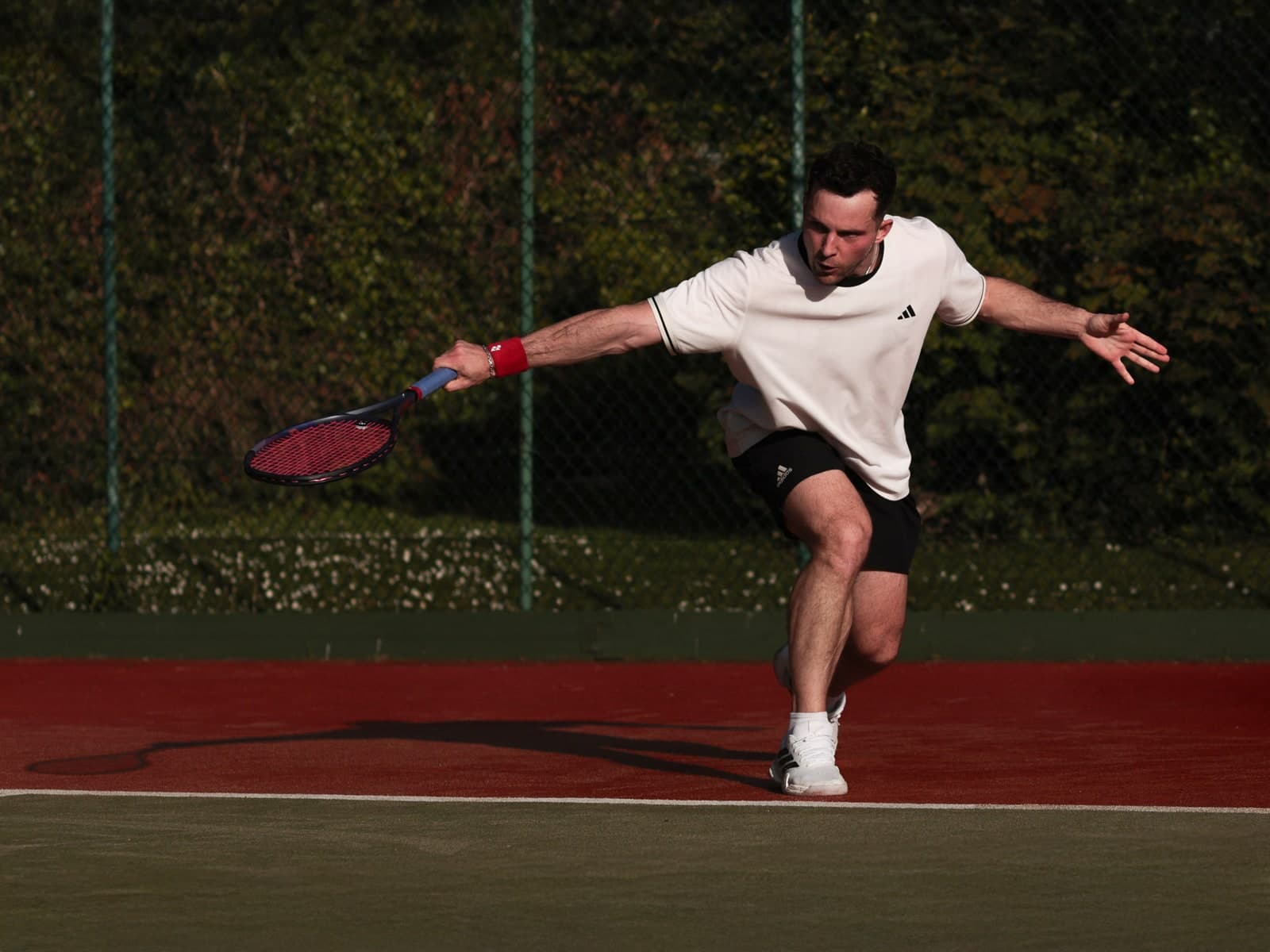 Stretching wide for a shot on a tennis court in a white T-shirt