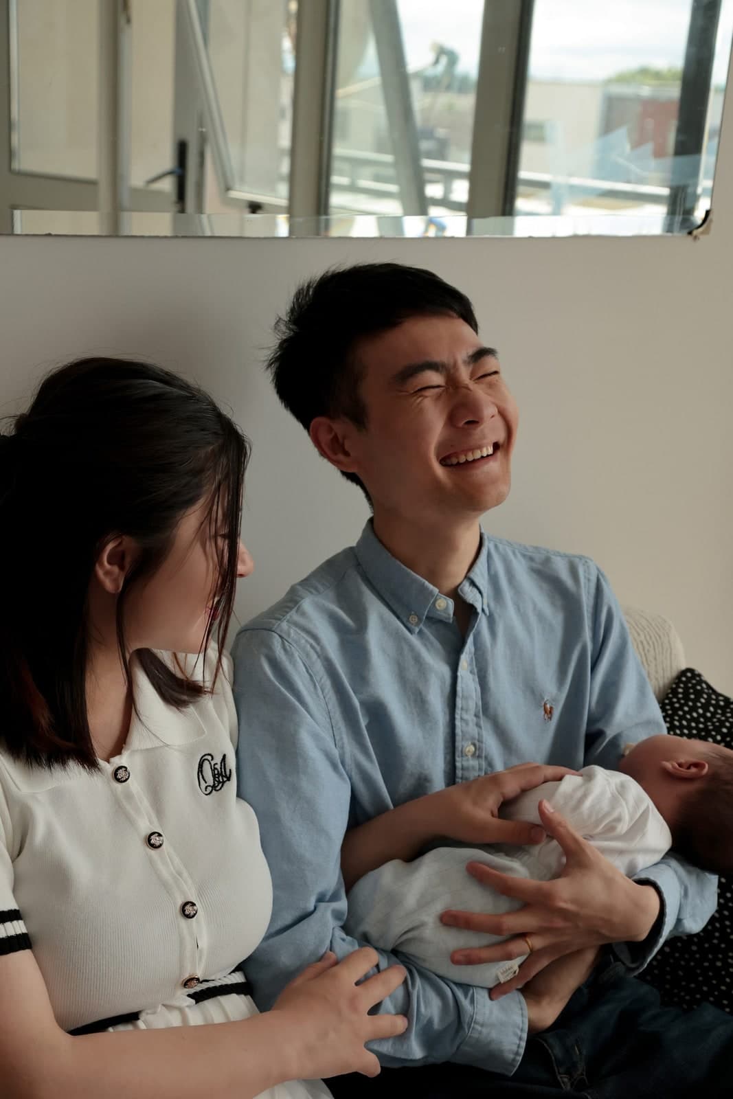 Parents laughing together at home, their newborn in one parent's arms